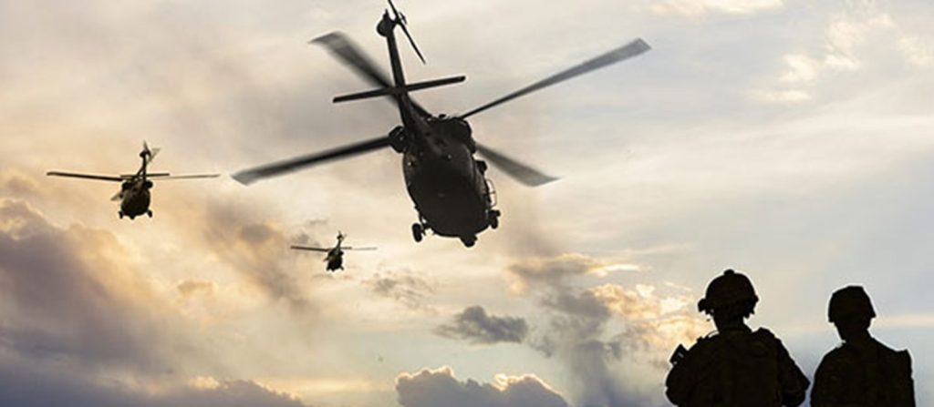 Helicopters fly over soldiers into the distance
