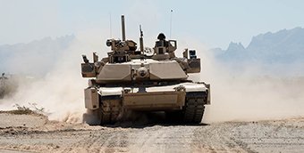 An Abrams tank with Trophy system drives on a dirt road.