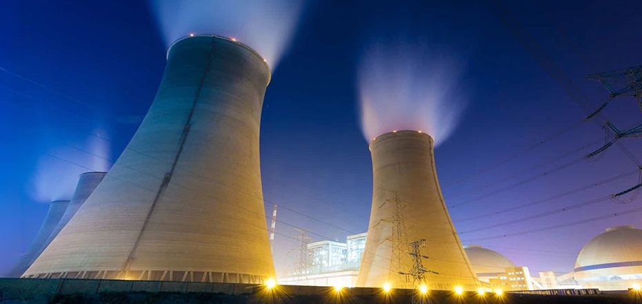 Nuclear power plant at night with illuminated cooling towers emitting steam.