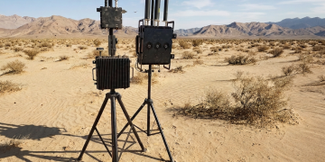 Two portable radio frequency systems with multiple antennas deployed on tripods in a desert environment.