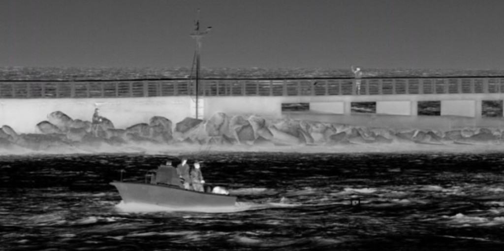 Small boat traveling through cold, turbulent water near a snow-covered shoreline, captured with thermal imaging.