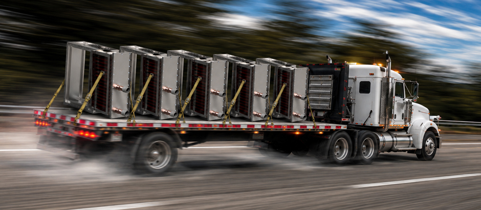 Flatbed semi-truck transporting multiple industrial equipment units along a highway.